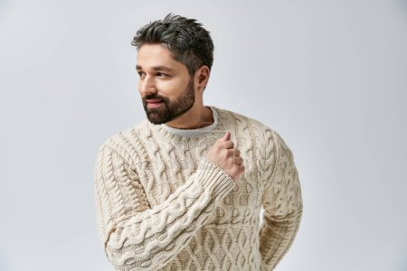 A charismatic man with a beard strikes a pose in a white sweater against a grey studio backdrop.