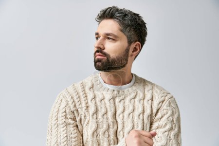 A charismatic man with a beard strikes a pose in a white sweater against a grey studio background.