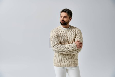 Photo for A stylish man with a beard striking a pose in a white sweater against a grey studio backdrop. - Royalty Free Image