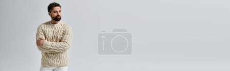 Photo for A charismatic man with a beard is posing in a white sweater against a grey studio background. - Royalty Free Image