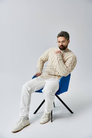 Téléchargez les photos : Un homme barbu dans un pull blanc assis sur une chaise, profondément dans la pensée avec sa main sur le menton. - en image libre de droit