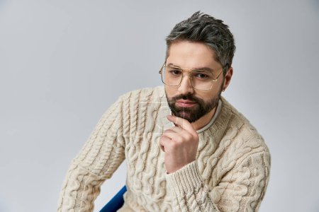 Photo for A bearded man in glasses wears a white sweater, exuding charm and intellect against a grey studio backdrop. - Royalty Free Image