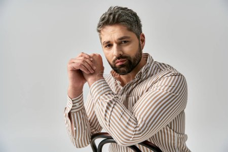 Foto de Un hombre elegante con barba se sienta en una silla, apoyando tiernamente su mano sobre su hombro. - Imagen libre de derechos