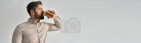 Téléchargez les photos : Un homme habillé d'une barbe dégustant un verre dans une tasse en papier sur fond gris - en image libre de droit