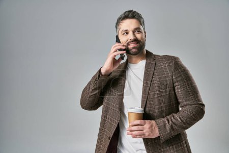 Téléchargez les photos : Un homme à la mode en tenue élégante tenant une tasse de café tout en parlant sur un téléphone portable. - en image libre de droit