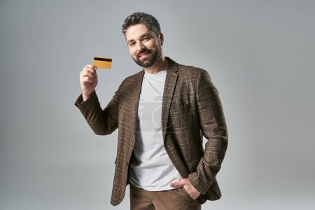 Bearded man in elegant attire confidently holds up a credit card, showcasing modern financial transactions.