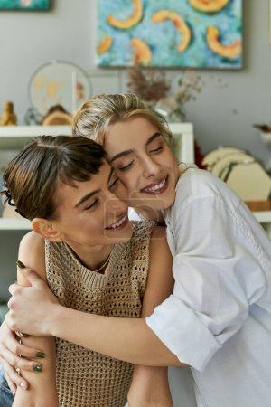 Two women, a loving lesbian couple, share a tender hug in an art studio.