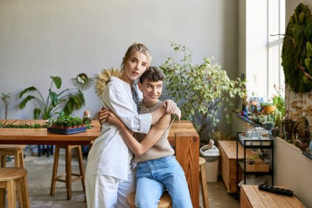 Téléchargez les photos : Two women in an art studio, one embraces the other lovingly amidst lush plants. - en image libre de droit
