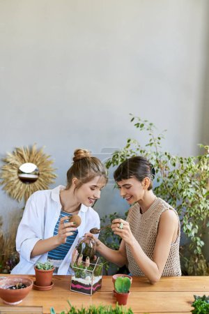 Two women, sharing a moment at a table surrounded by plants in an art studio.