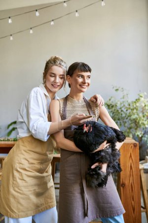 Zwei Frauen halten in einem Kunstatelier zärtlich ein Huhn in der Hand.