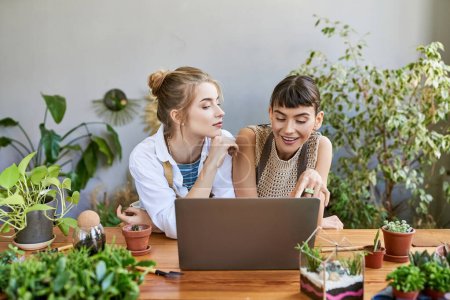 Photo for Two women, a loving lesbian couple, sit at a table, absorbed in a laptop screen at an art studio. - Royalty Free Image
