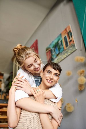 Foto de Abrazo tierno entre dos mujeres, una sosteniendo a la otra en sus brazos en un estudio de arte. - Imagen libre de derechos