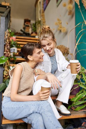 Zwei Frauen genießen Kaffee auf einer Bank in einem Kunstatelier.