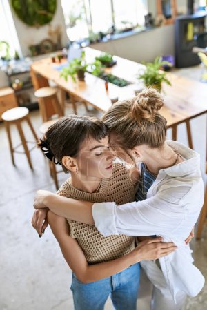 Two women warmly hug each other in a cozy kitchen setting.