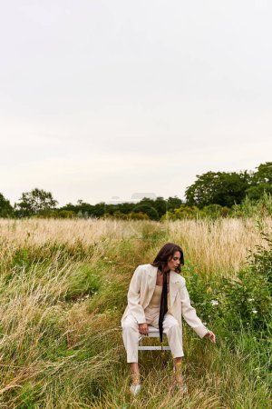 Eine junge Frau in weißer Kleidung sitzt auf einem Stuhl in einem ruhigen Feld und sonnt sich in der warmen Sommerbrise.