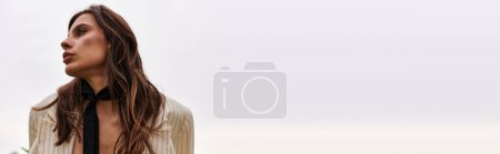 Foto de Una hermosa joven con el pelo largo emana elegancia en una corbata negra, contrastando con la brisa del verano en un campo pintoresco. - Imagen libre de derechos