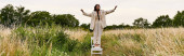 A young woman in white attire stands on a chair, embracing the summer breeze in a peaceful field. magic mug #715529034