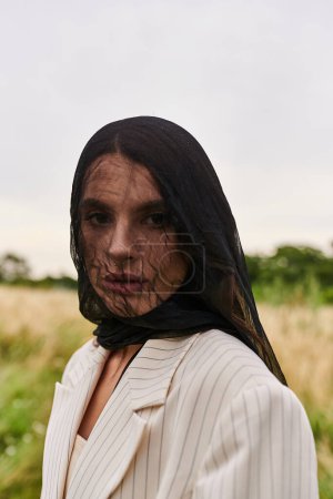 Téléchargez les photos : Une belle jeune femme en costume blanc et écharpe noire, profitant de la brise estivale dans un champ de nature. - en image libre de droit