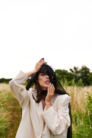 Eine schöne junge Frau in weißem Gewand steht mit einem Schleier, der in der Sommerbrise in einem ruhigen Feld weht.