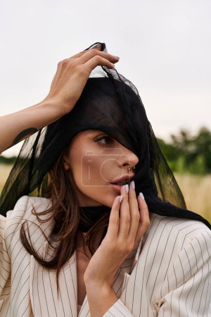 Foto de A young woman in white attire enjoying the summer breeze in a field, her head adorned with a delicate veil. - Imagen libre de derechos