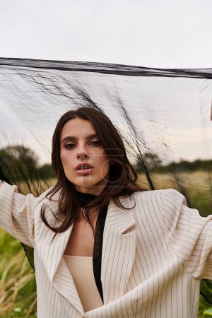 Téléchargez les photos : Une jeune femme élégante dans une veste blanche tient un voile noir sous la pluie dans un cadre naturel serein. - en image libre de droit