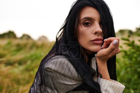 Una hermosa joven con el pelo negro usando una bufanda, disfrutando de la brisa del verano en un campo pintoresco.