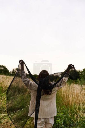 Photo for A beautiful young woman in white attire strolling through a field, tenderly clutching a black net under the summer sky. - Royalty Free Image