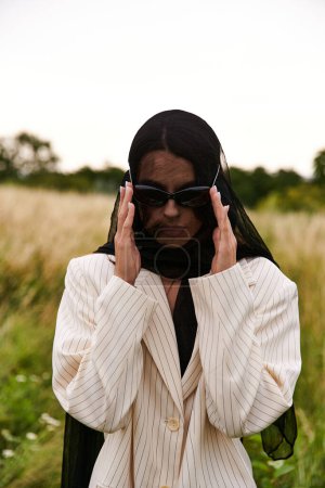 A stylish woman in a suit and sunglasses stands confidently in a vast field, embodying grace and sophistication in nature.
