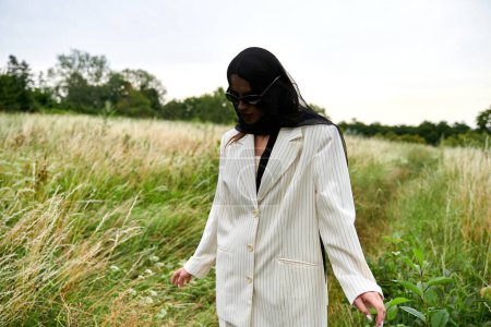 A beautiful young woman in a white suit gracefully walks through tall grass in a serene field, enjoying the summer breeze.
