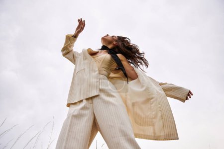 Eine schöne junge Frau im weißen Anzug fliegt anmutig durch die Luft und umarmt die sommerliche Brise auf einem ruhigen Feld.