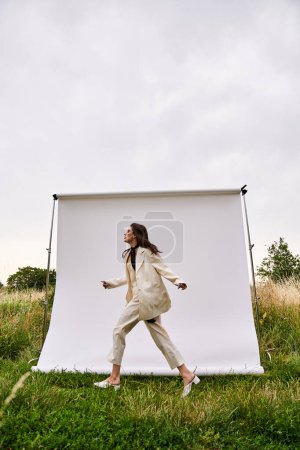 Téléchargez les photos : Une belle jeune femme en tenue blanche se tient paisiblement dans un champ ensoleillé, profitant de la douce brise d'été. - en image libre de droit