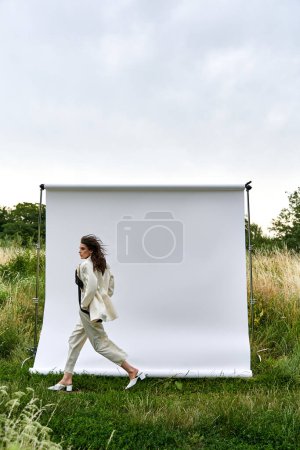 Photo for A beautiful young woman in white attire walks gracefully in front of a white backdrop, exuding elegance and serenity. - Royalty Free Image