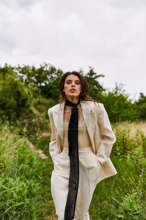 A stylish woman clad in a suit and tie stands confidently in a sunlit field, embracing the beauty of nature around her.