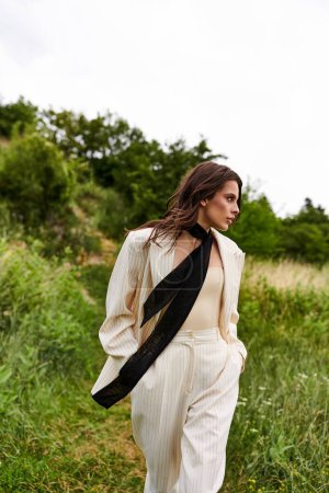 Una hermosa joven con un traje blanco y una bufanda negra disfruta de la brisa del verano en un campo sereno.