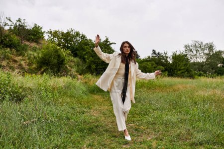 Eine schöne junge Frau im weißen Mantel geht anmutig durch ein friedliches Feld und genießt die sommerliche Brise.