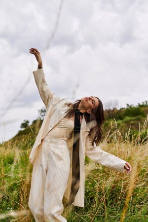 Foto de Una hermosa joven vestida de blanco de pie en un campo de hierba alta, sintiendo la brisa del verano en su cara. - Imagen libre de derechos