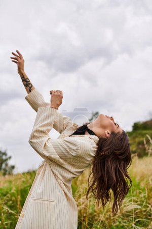 Eine schöne junge Frau in weißem Gewand steht anmutig auf einem Feld aus hohem Gras und spürt die Sommerbrise.