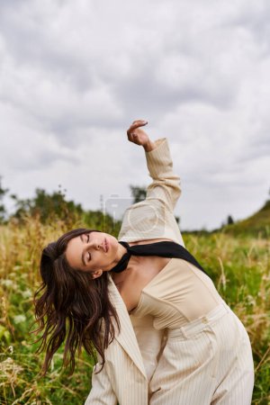 Foto de Una hermosa joven con un traje blanco y corbata negra disfrutando de la brisa del verano en un campo. - Imagen libre de derechos