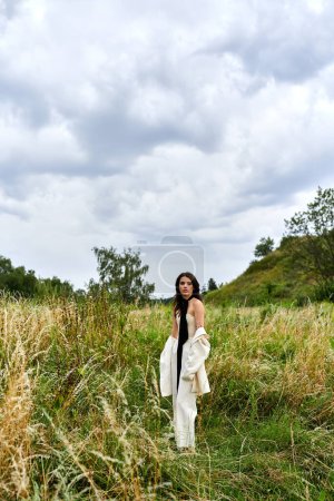 Eine schöne junge Frau in weißem Gewand genießt die Sommerbrise in einem Feld mit hohem Gras.