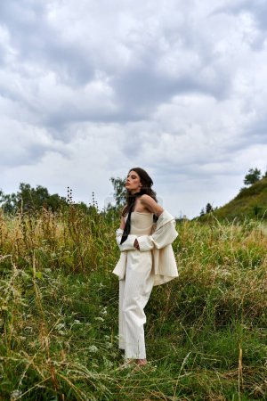 Eine schöne junge Frau in weißem Gewand steht anmutig auf einem Feld aus hohem Gras und genießt die Sommerbrise.