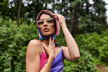Foto de A young woman, dressed vibrantly, enjoying a summer breeze with a scarf around her head. - Imagen libre de derechos