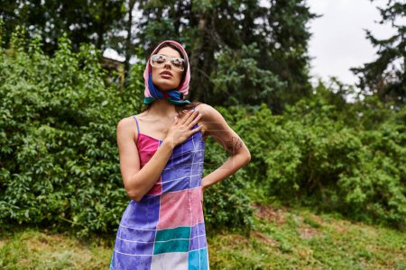 Téléchargez les photos : Une jeune femme vibrante portant une serviette colorée se tient gracieusement dans un champ ensoleillé, incarnant la joie et la beauté dans la nature. - en image libre de droit