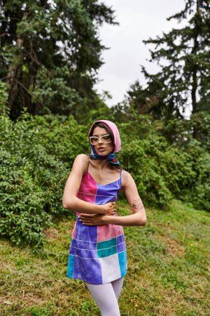 Téléchargez les photos : Une jeune femme dans une robe colorée et des lunettes de soleil dansant gracieusement dans un champ animé, profitant de la brise d'été. - en image libre de droit