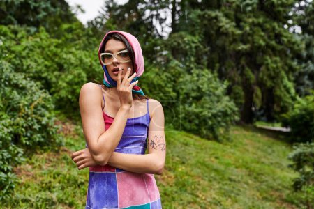 Téléchargez les photos : Jeune femme profitant de la brise d'été dans la nature, vêtue d'une robe vibrante et portant des lunettes de soleil élégantes. - en image libre de droit