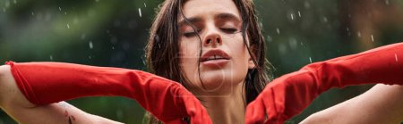 Téléchargez les photos : Une jeune femme en gants longs rouges se tient debout avec confiance, les mains sur les hanches, embrassant la pluie. - en image libre de droit