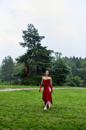 Foto de Una joven atractiva con un vestido rojo y guantes largos de pie con gracia en un campo, abrazando la brisa del verano. - Imagen libre de derechos
