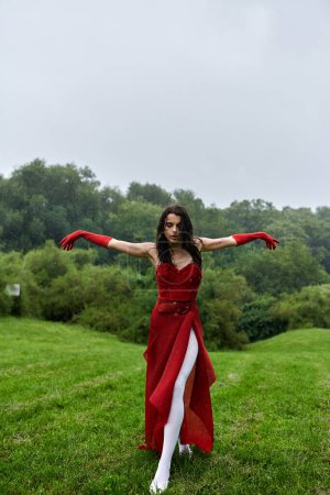 A captivating young woman in a red dress and long gloves standing gracefully in a beautiful field, relishing the summer breeze.
