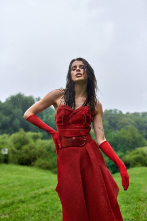 Eine junge Frau in einem scharlachroten Kleid und langen Handschuhen steht anmutig in einem weiten Feld und umarmt die sanfte Sommerbrise.