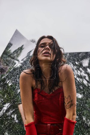 Una escena fascinante se desarrolla como una mujer joven con un vestido rojo llamativo y guantes largos se levanta con gracia sobre un telón de fondo de una montaña.