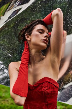 Una joven con un llamativo vestido rojo y guantes largos, disfrutando de la brisa veraniega en la naturaleza.